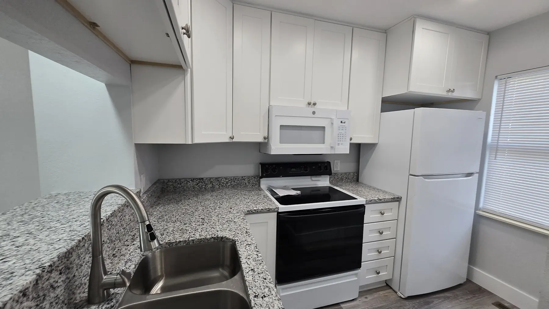 Renovated kitchen with white appliances and granite counters in Unit 103